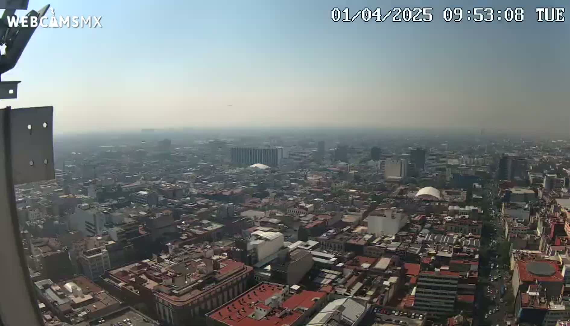 A hazy, high-angle view shows a sprawling city under a clear, bright sky.