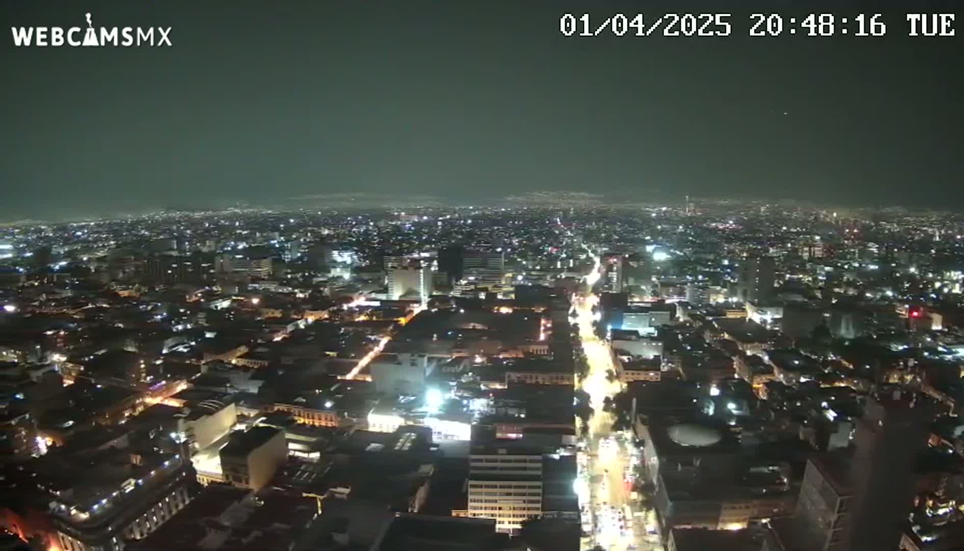 A nighttime aerial view of a sprawling city with many illuminated buildings and streets.