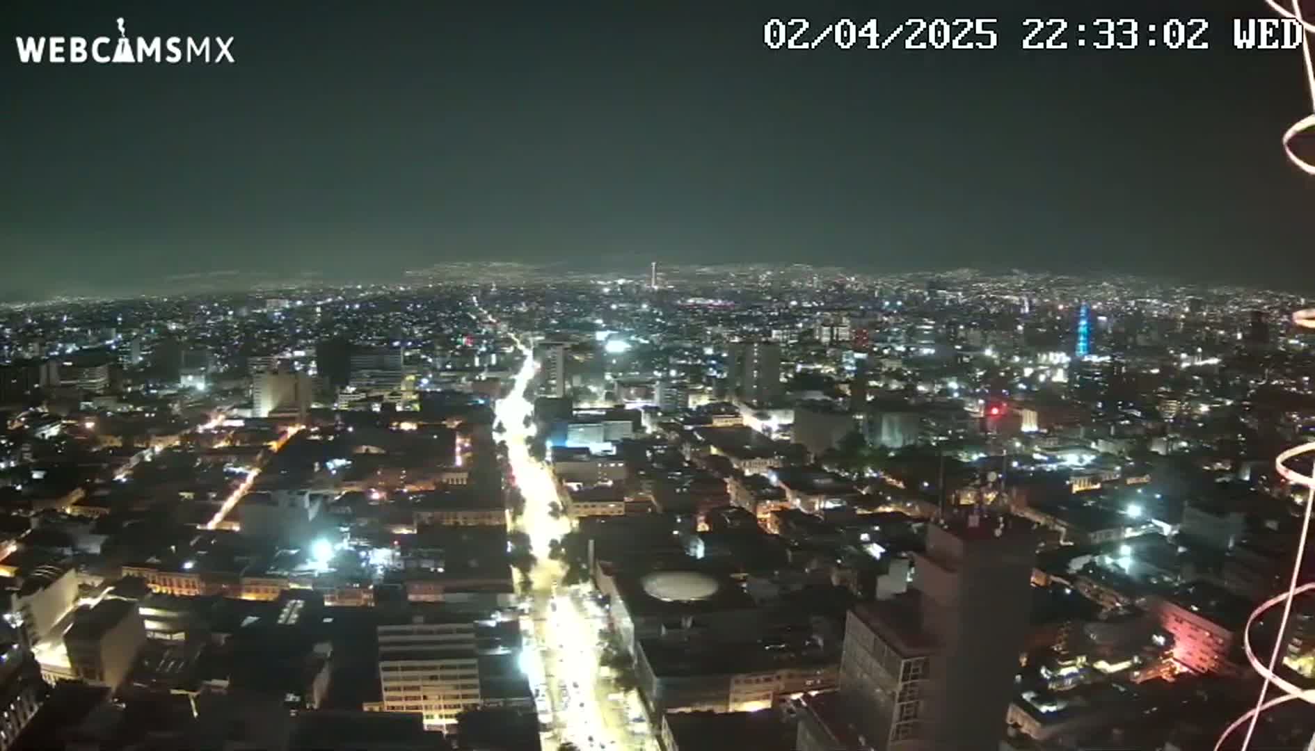 A nighttime, high-angle view of a sprawling city with brightly lit streets and buildings under a clear sky.