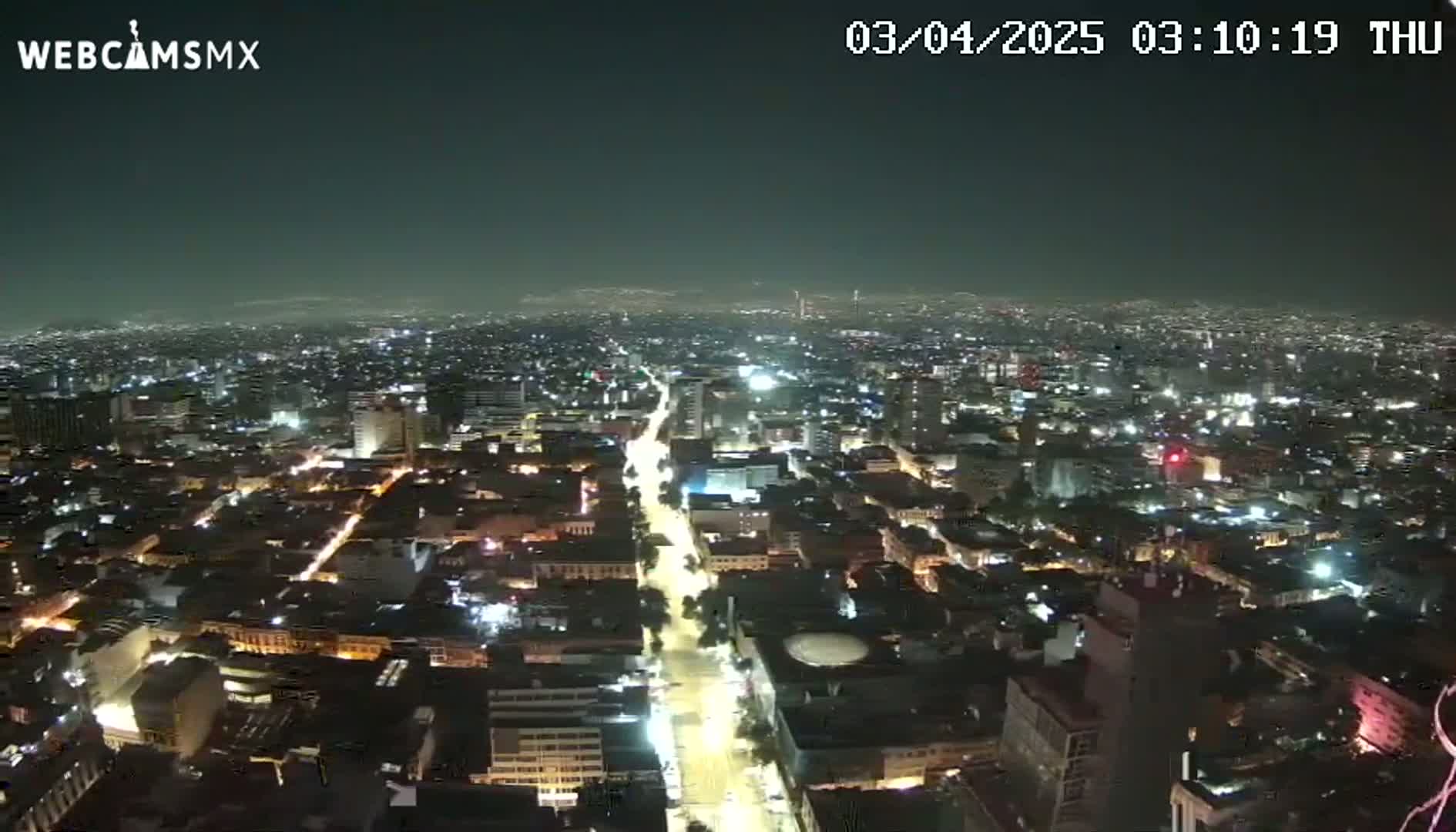 A nighttime, high-angle view of a sprawling city illuminated by streetlights and building lights under a dark, clear sky.