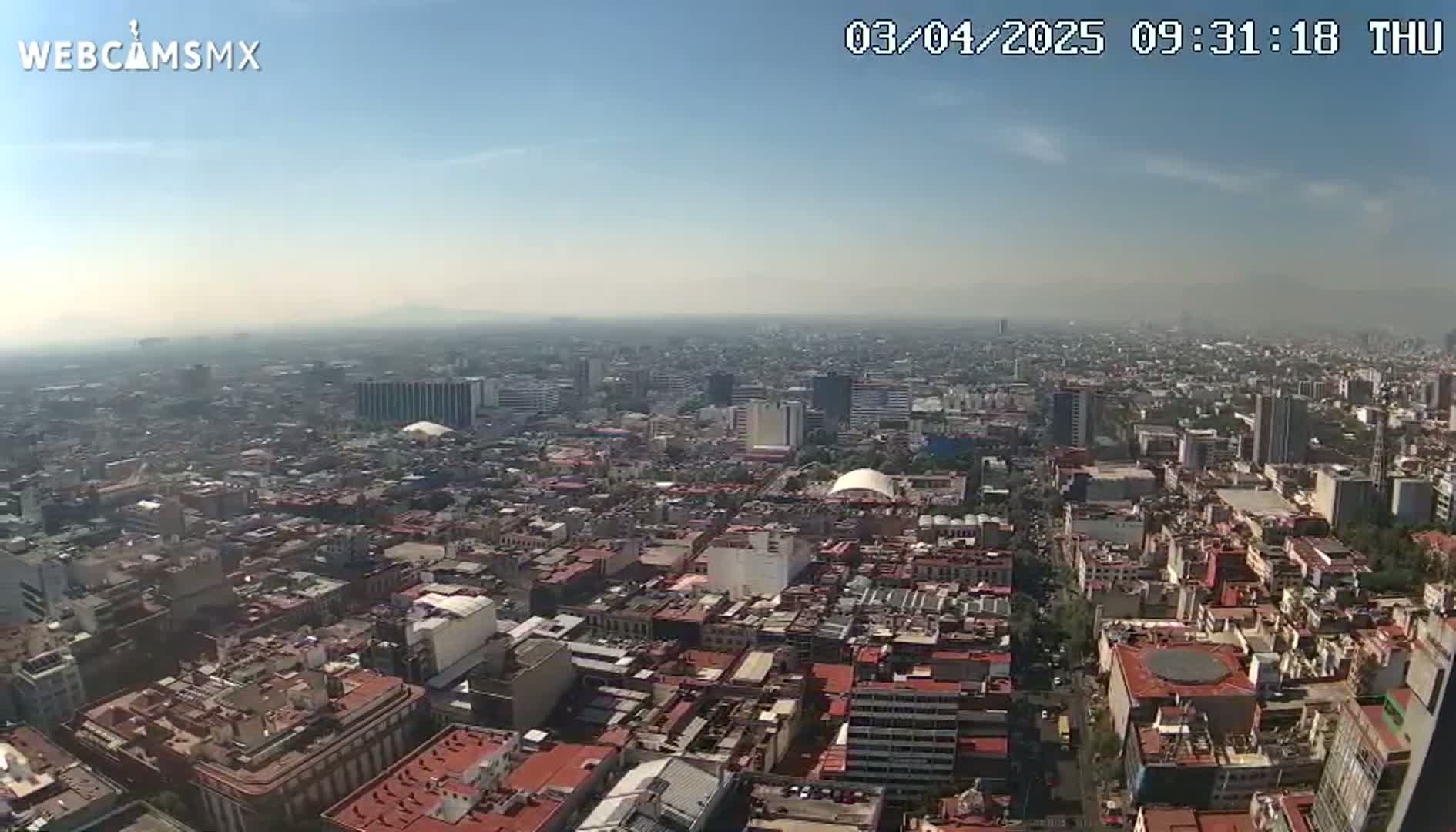 A hazy, sunny day reveals a sprawling cityscape of dense buildings stretching to the horizon.