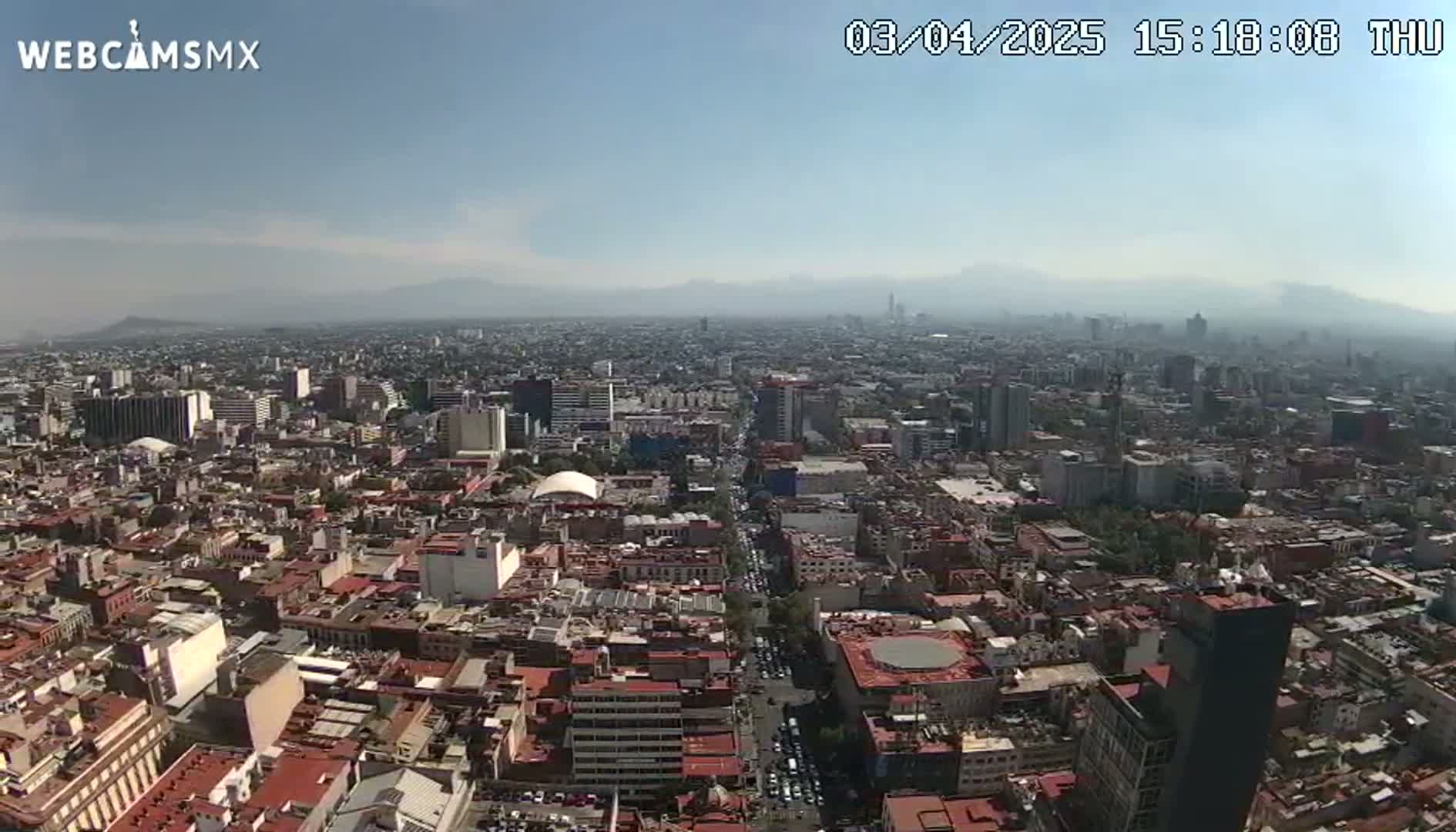 A hazy, sunny day reveals a sprawling cityscape, with distant mountains visible on the horizon.