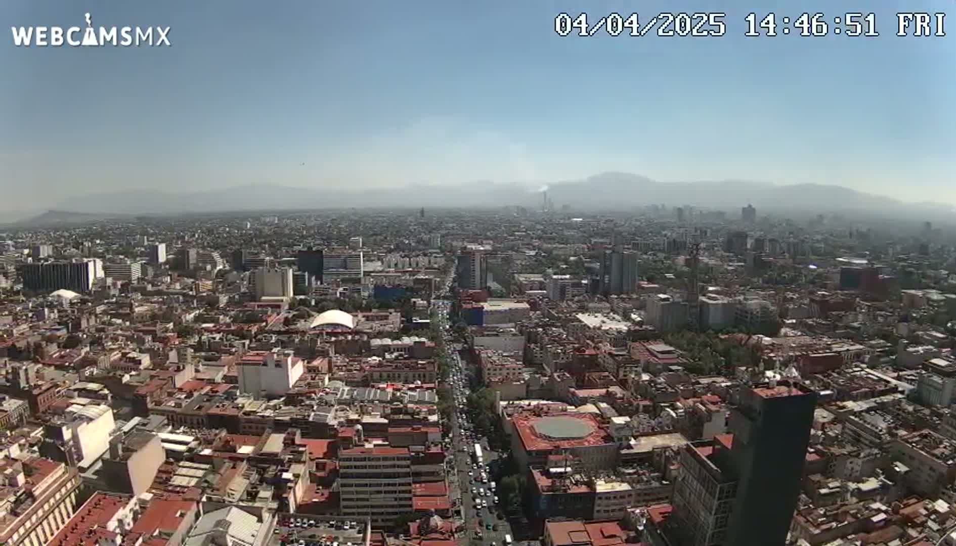 A hazy, sunny day reveals a sprawling cityscape with numerous buildings, streets, and distant mountains.