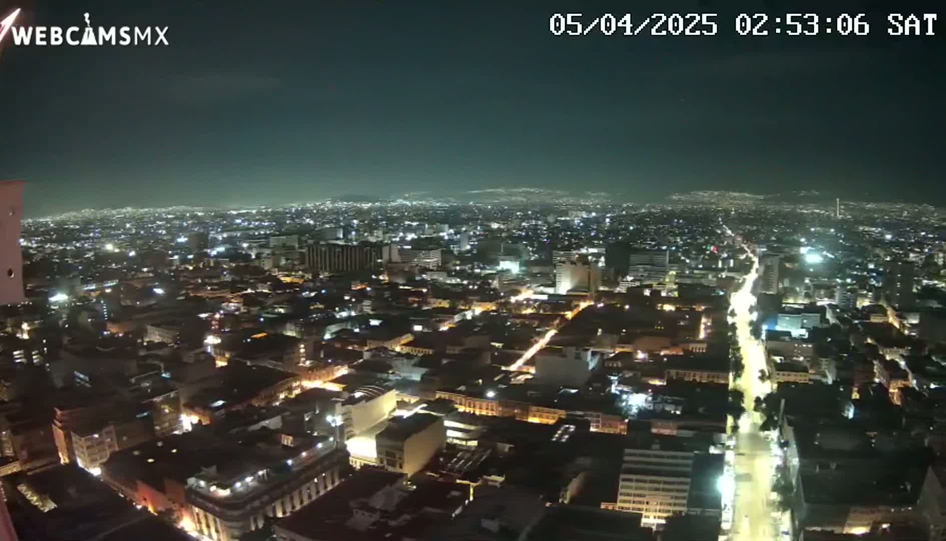 A nighttime aerial view of a sprawling city illuminated by streetlights and building lights under a clear sky.