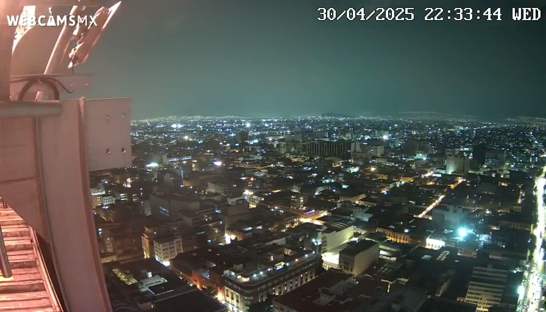 A nighttime, high-angle view of a sprawling city illuminated by numerous lights, seen from a tall structure.