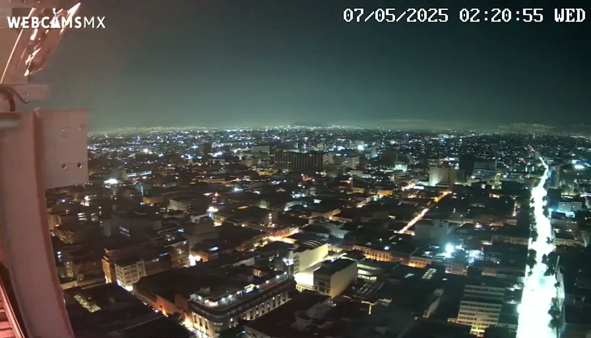 A nighttime, high-angle view shows a sprawling city illuminated by streetlights and building lights under a clear, dark sky.