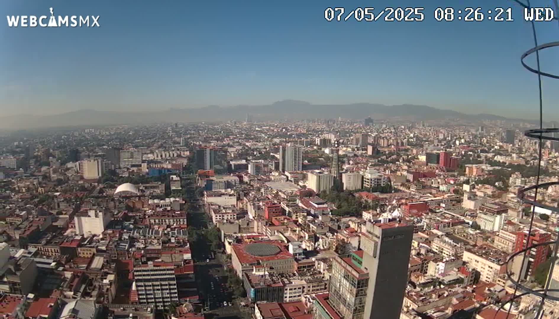 A hazy, sunny day reveals a sprawling cityscape extending to distant mountains.
