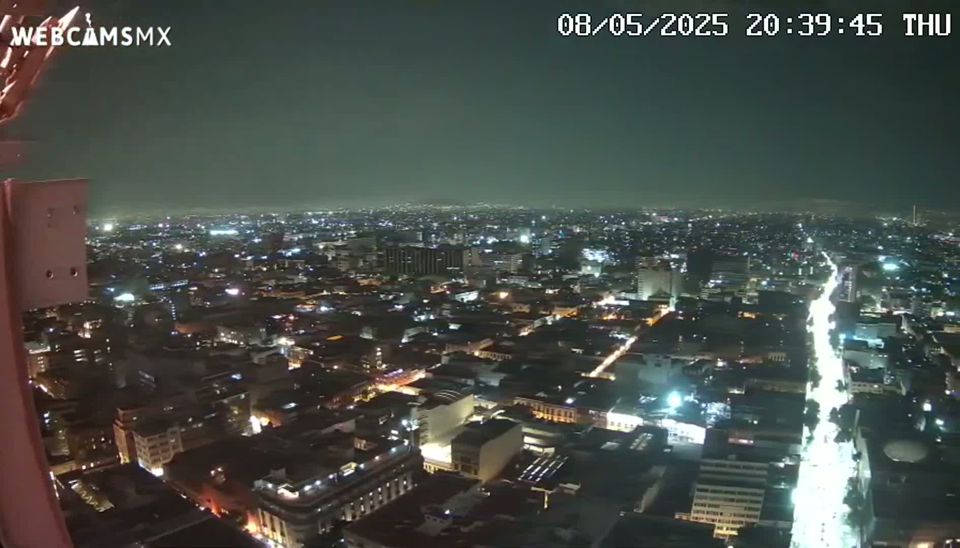 A nighttime, high-angle view of a sprawling city with brightly lit streets and buildings.