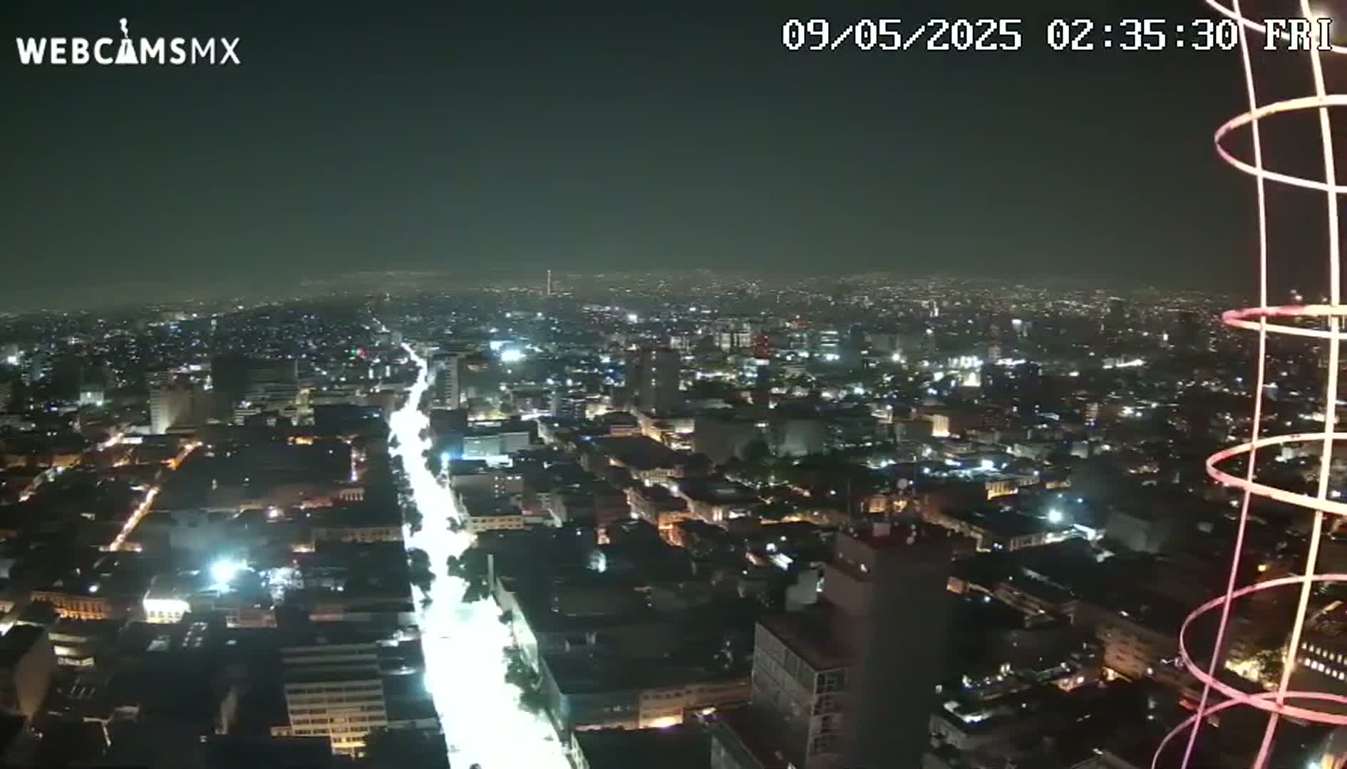 A nighttime, high-angle view of a sprawling city with brightly lit streets and buildings, under a hazy sky.