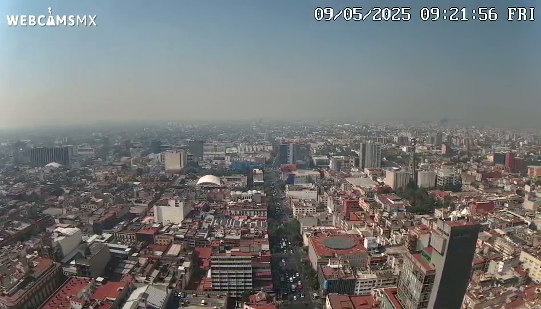 A hazy, high-angle view shows a sprawling cityscape with densely packed buildings under a clear sky.