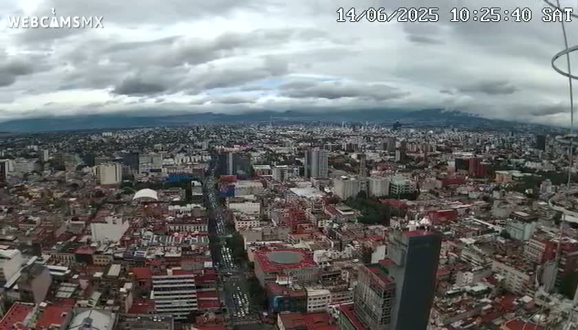 A sprawling city under a cloudy sky stretches to distant mountains.