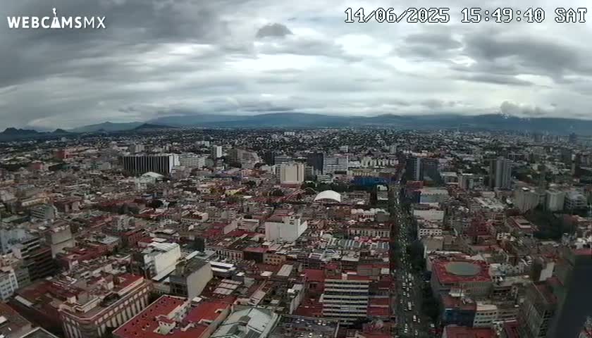 A sprawling city under a cloudy sky stretches to distant mountains.