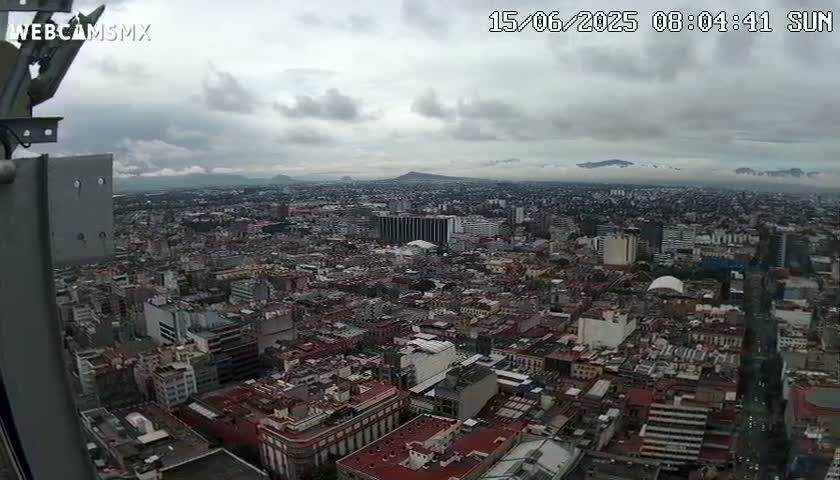A high-angle, long shot of a sprawling city under a cloudy sky shows distant mountains in the background.