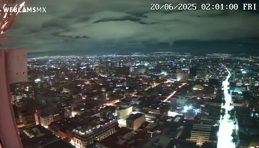 A nighttime, high-angle view of a sprawling city illuminated by numerous lights under a cloudy sky.