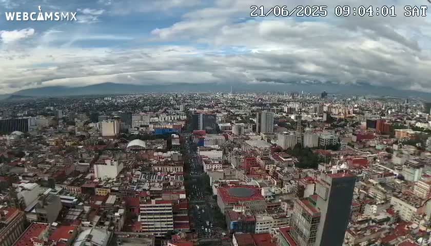 An expansive view of a densely populated city under a partly cloudy sky, with mountains visible in the distance.