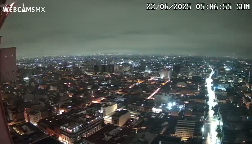 A nighttime, overcast view of a sprawling city with brightly lit streets and buildings.