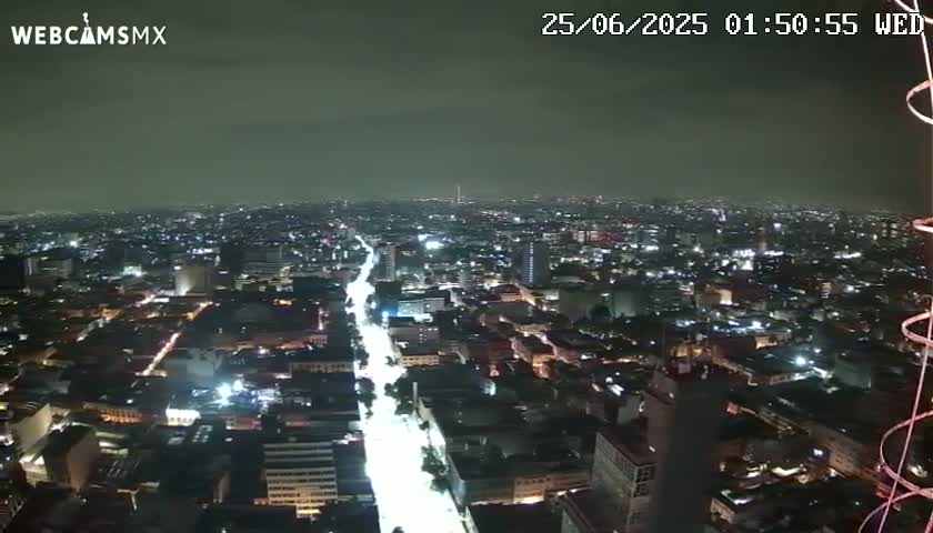 A nighttime aerial view of a sprawling city with brightly lit streets and buildings under a cloudy sky.