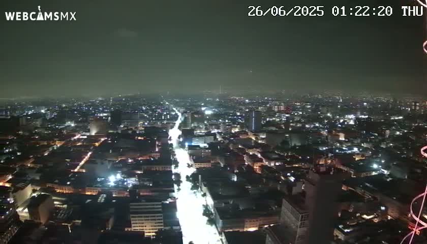 A nighttime, high-angle view of a city with brightly lit streets and buildings under a hazy sky.