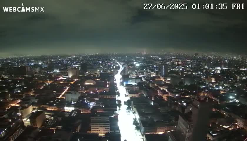 A nighttime aerial view of a brightly lit city under a cloudy sky.