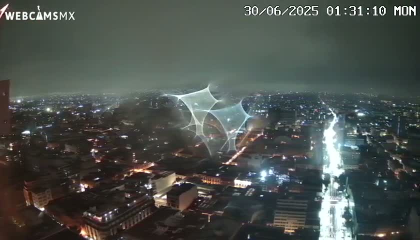 A nighttime, hazy view of a city illuminated by streetlights, with a large, light-based structure or projection visible in the center.