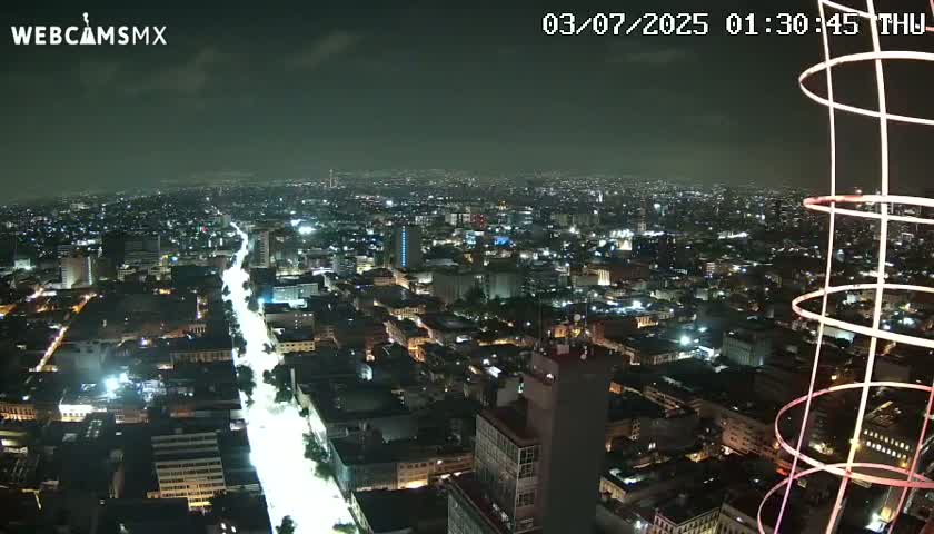 A nighttime aerial view of a brightly lit city with a long, illuminated road cutting through it, under a mostly clear sky.