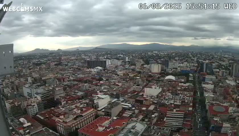 A high-angle view of a sprawling city under a cloudy sky, with distant mountains visible on the horizon.