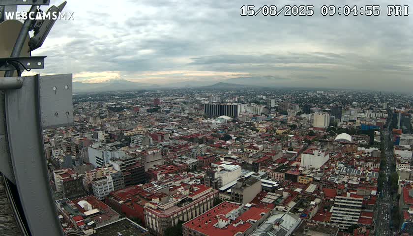 A high-angle view of a sprawling city under a cloudy sky, with distant mountains visible on the horizon.