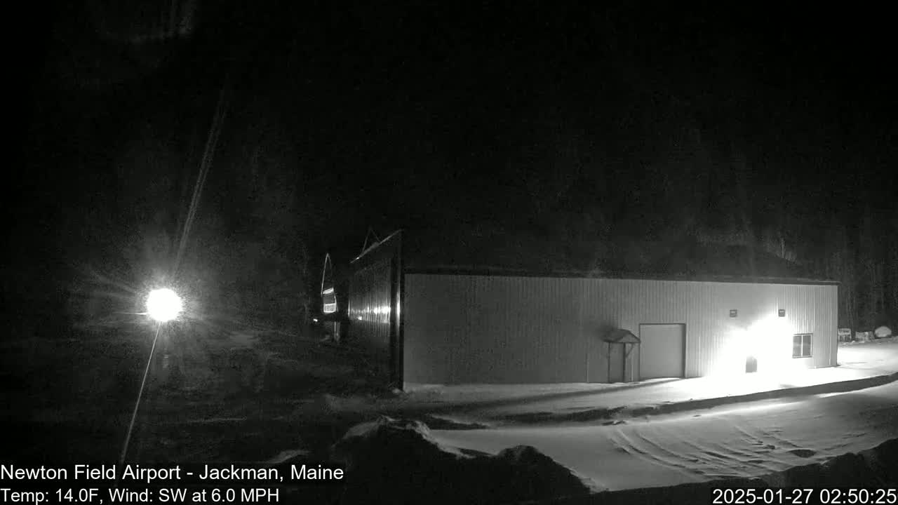 A snow-covered landscape at night shows a long, rectangular building lit from within, under a dark sky with a southwest wind.