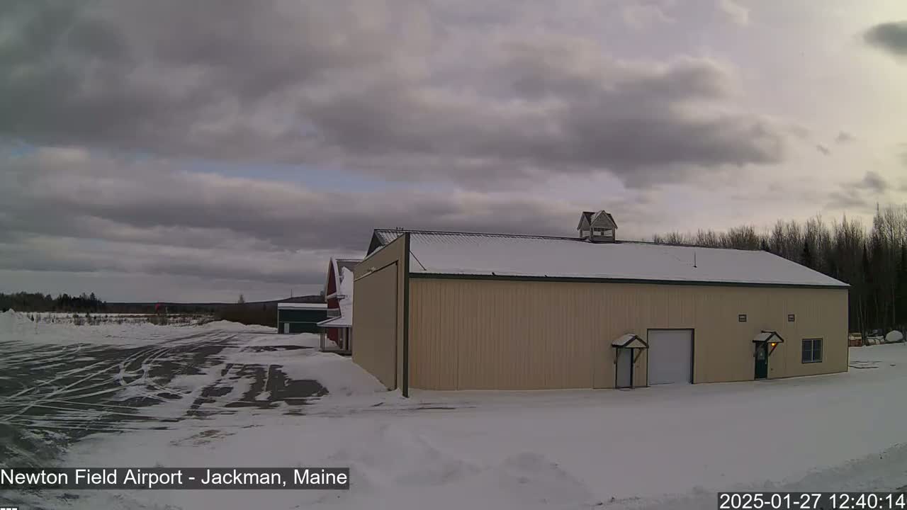 A large tan hangar sits in a snowy airfield under a cloudy sky.