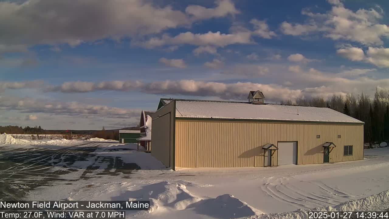 A large tan hangar sits in a snowy airfield under a partly cloudy sky.