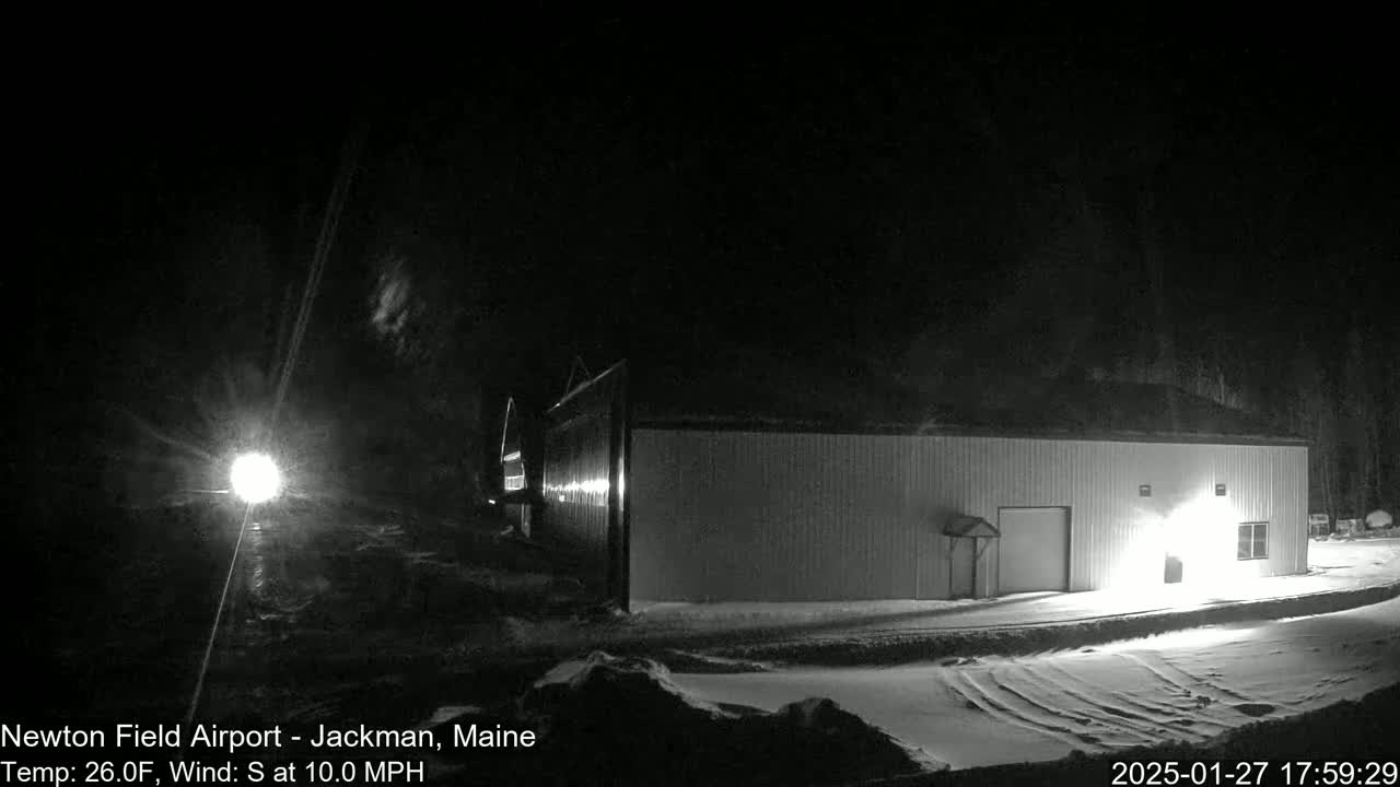 A long, light-colored building is illuminated at night in a snowy landscape under a dark sky with a 10 mph south wind and a temperature of 26°F.
