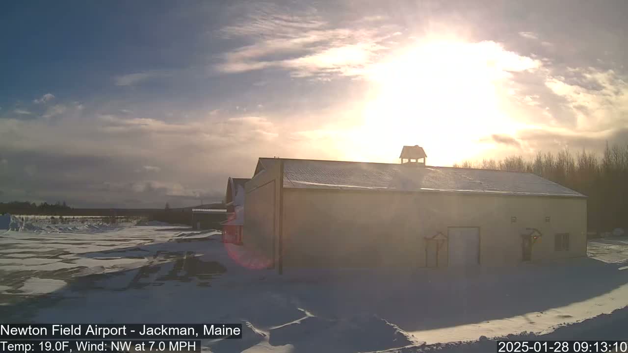 A snow-covered, light-beige building stands in a snowy landscape under a partly sunny sky.