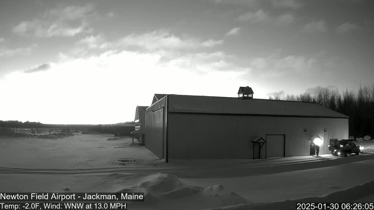 A large, dark building stands in a snow-covered landscape under a mostly cloudy, brightening sky with a wind of 13 mph.