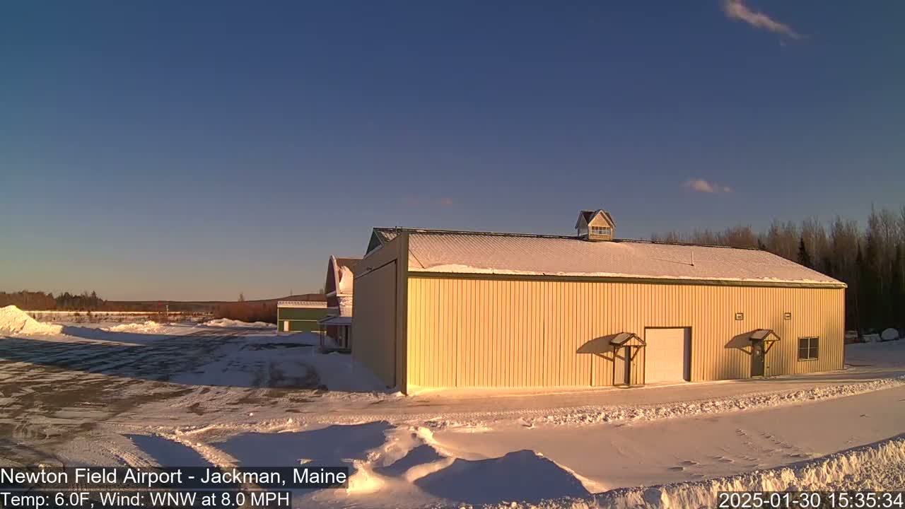 A large, tan building with a snow-covered roof sits in a snowy, outdoor setting under a clear blue sky.