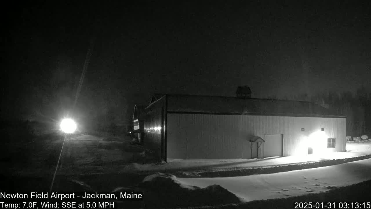 A long, light-colored building is illuminated at night in a snowy landscape under a dark sky.