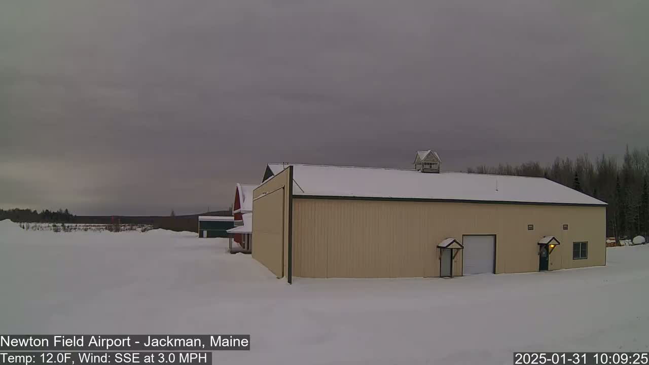 A large tan hangar sits in a snowy field under an overcast sky.
