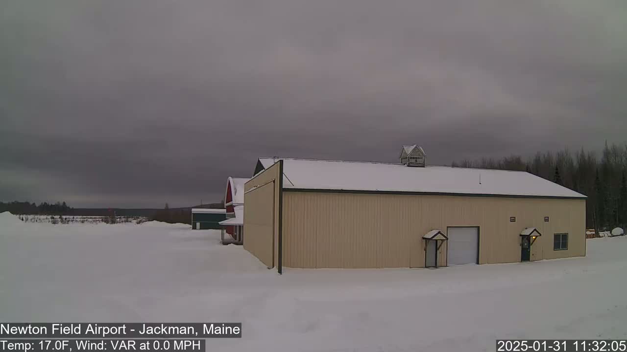 A large tan hangar sits in a snow-covered landscape under an overcast sky.