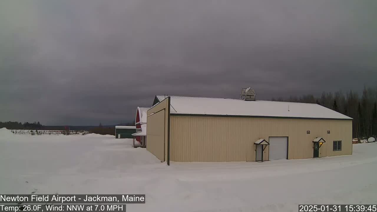 A tan hangar and a red barn sit on a snow-covered field under a gray, overcast sky.