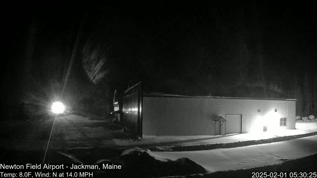 A long, low building is illuminated at night in a snowy landscape under a dark, windy sky.