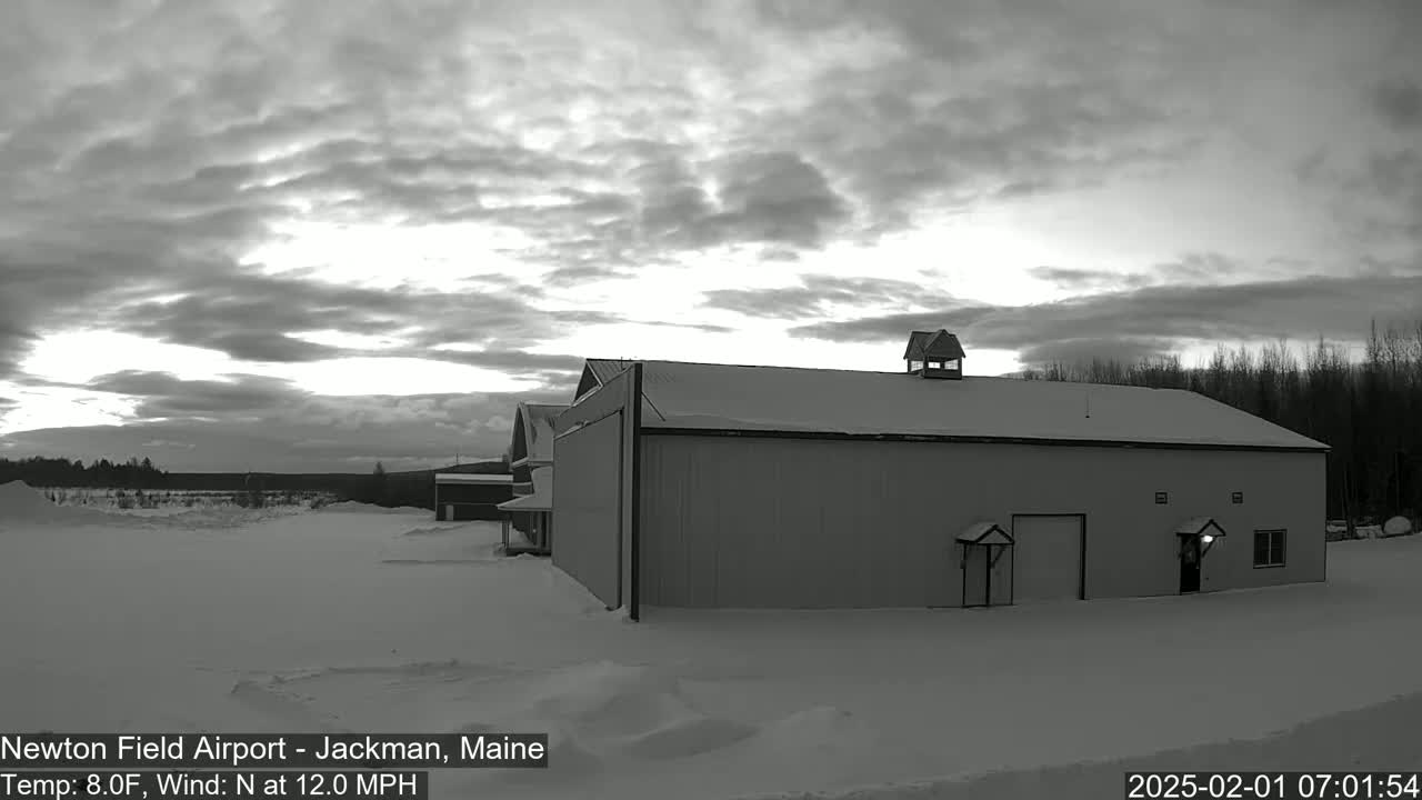 A large, snow-covered hangar sits in a snowy landscape under a cloudy, brightening sky.