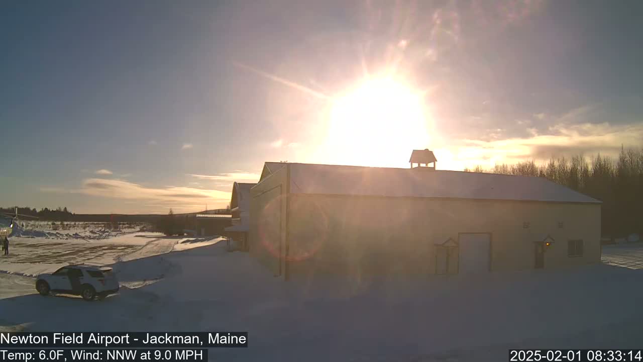 A large, tan building with a snow-covered roof sits in a snowy landscape under a bright, sunny sky.