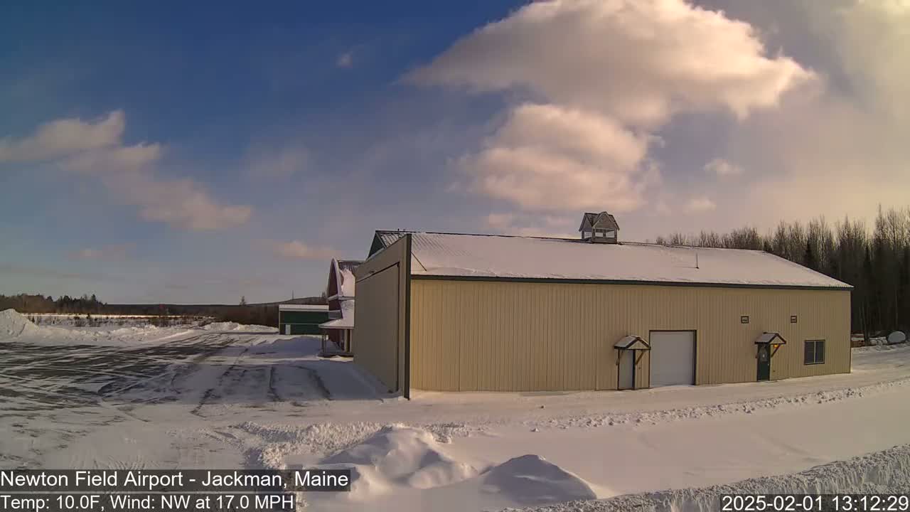 A large tan building with a snow-covered roof stands in a snowy landscape under a partly cloudy sky.
