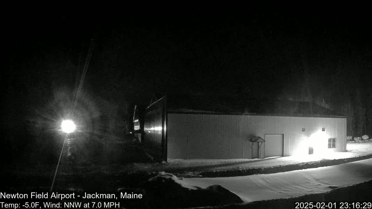 A long, single-story building is illuminated at night in a snowy area with a northwest wind.
