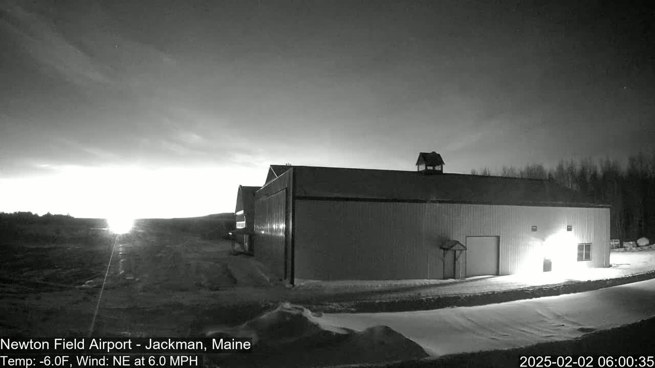 A large hangar sits on a snow-covered airfield at dawn under a mostly clear sky with a northeasterly wind.