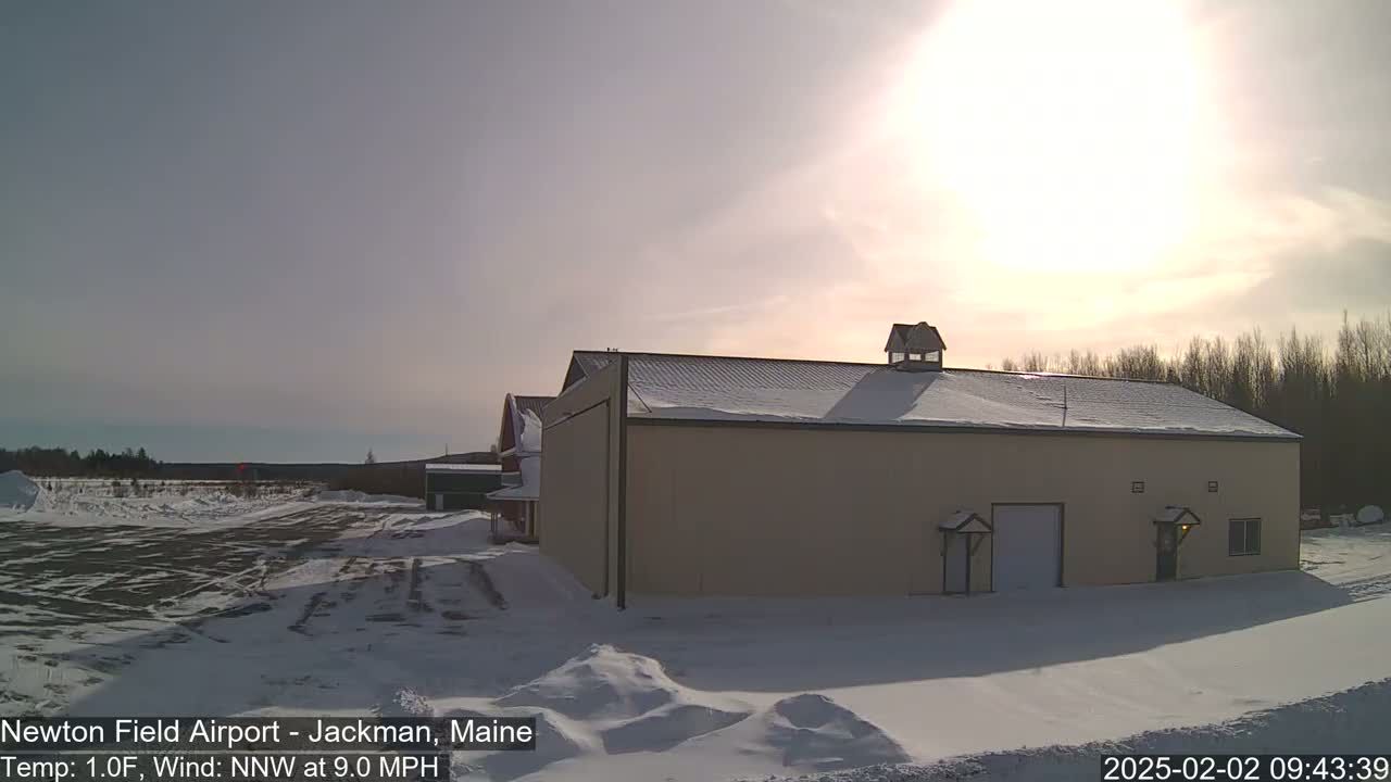 A tan building with a snow-covered roof stands in a snowy landscape under a bright, sunny sky.