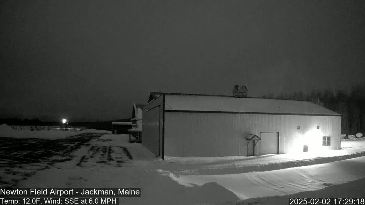 A large, light-colored building sits in a snow-covered area at night under a dark, overcast sky.