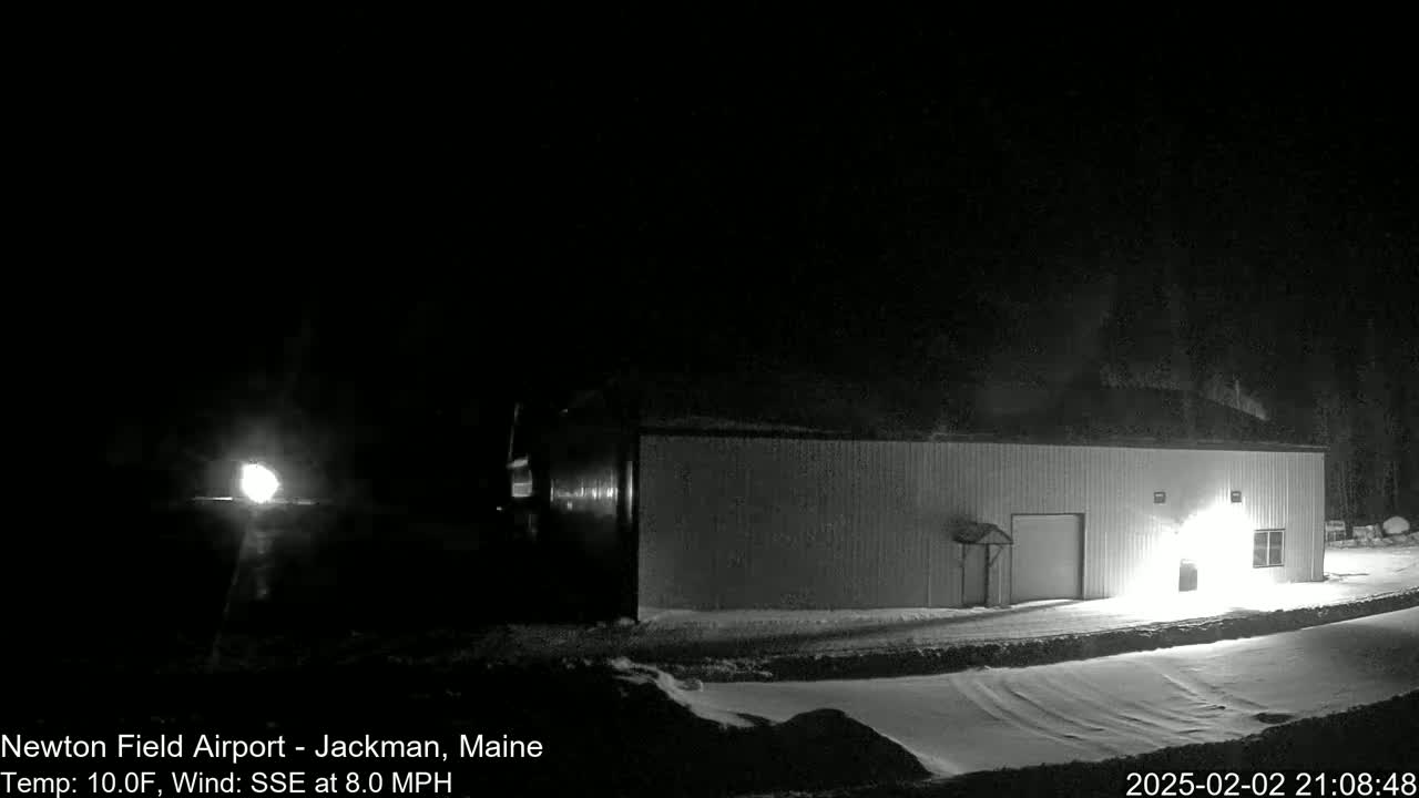 A long, low building sits in a snowy area at night, illuminated by lights, under a dark sky with a wind from the south-southeast at 8 miles per hour and a temperature of 10 degrees Fahrenheit.