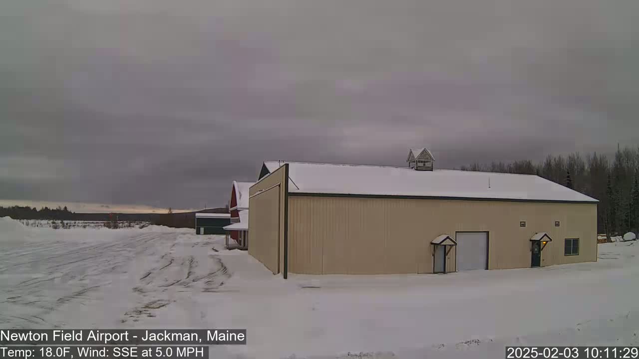 A tan hangar sits in a snow-covered field under an overcast sky with a light south-southeasterly wind.