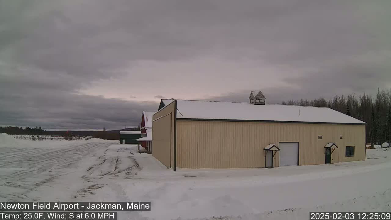 A tan hangar sits in a snow-covered airfield under an overcast sky.