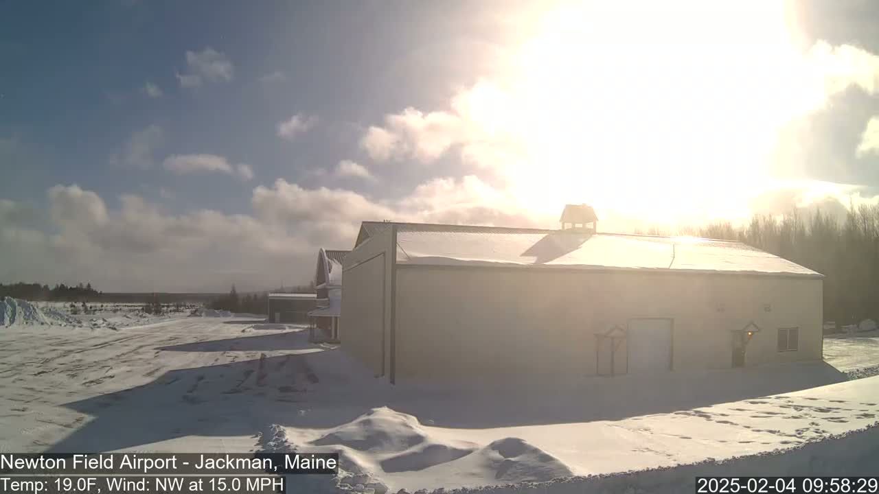 A snow-covered landscape with a large building is bathed in bright sunlight under a partly cloudy sky.